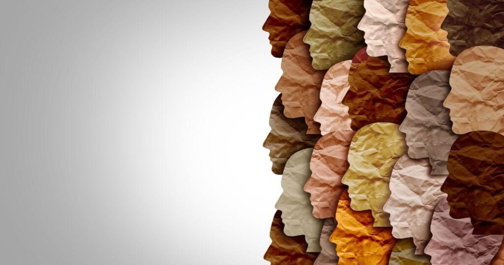 Paper cut outs of face silhouettes in multiple colors to represent skin tones, on a gray background.