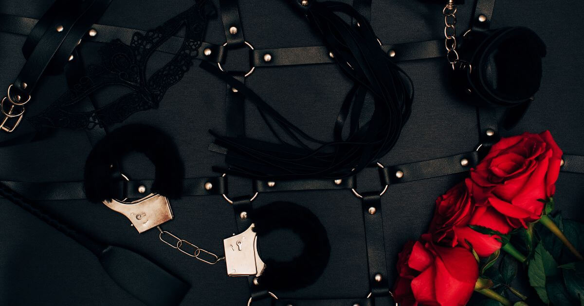 An image of a BDSM themed background. There are leather cuffs and roses.