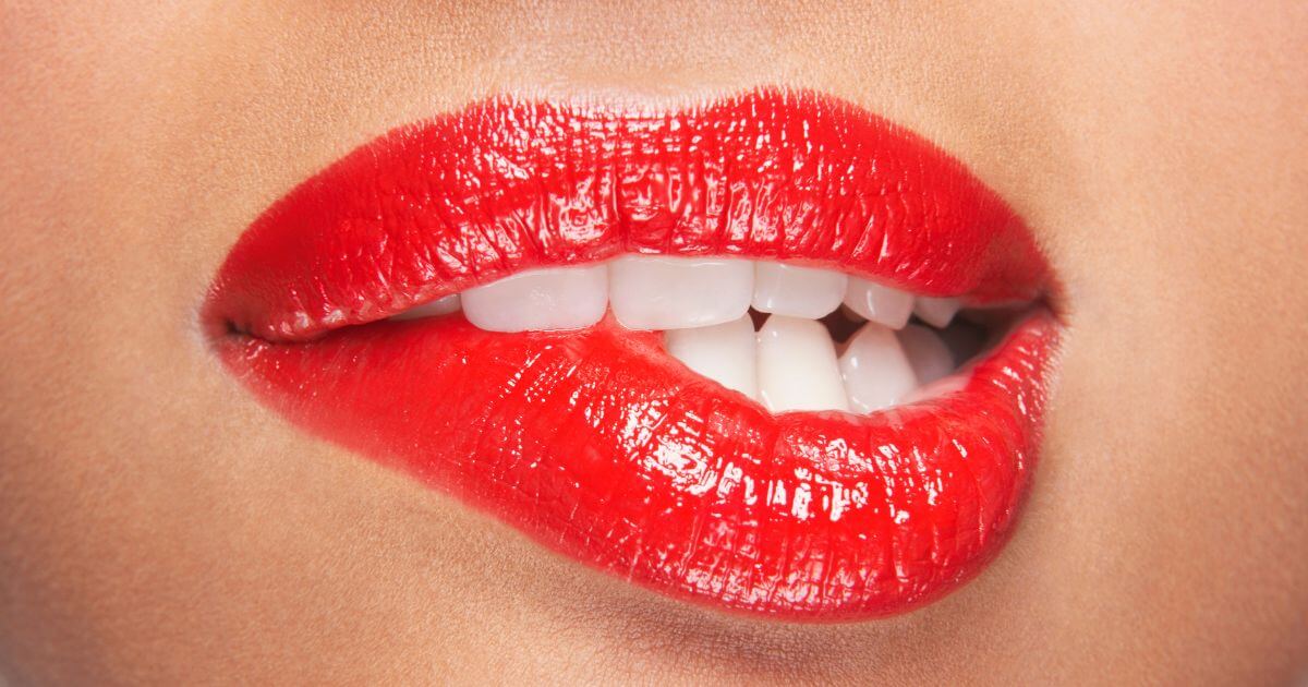 A woman with red lipstick on, biting her lower lip seductively.