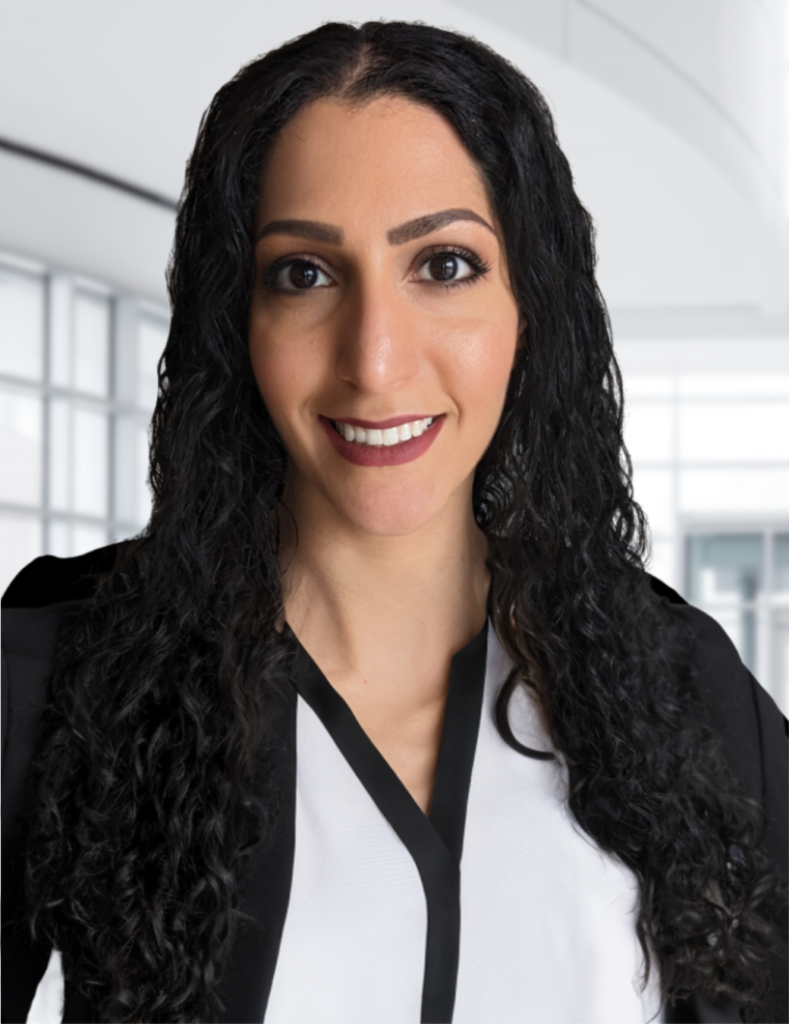 An image of Lilithfoxx in a professional blouse and blazer standing in a bright office building.