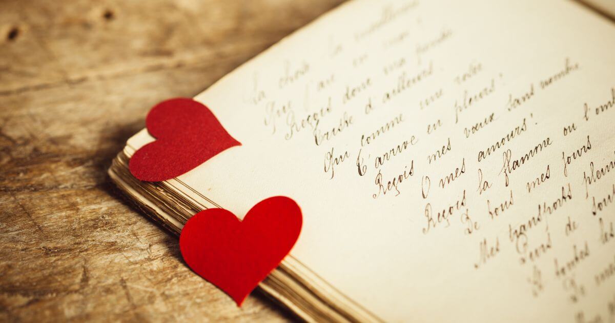An image of a journal with script writing and red paper cut out hearts on the corner of the journal.