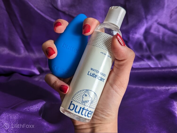 An image of Lilithfoxx holding a bottle of Butter Wellness water-based lubricant and The Personal Massager for prostate orgasm toy.