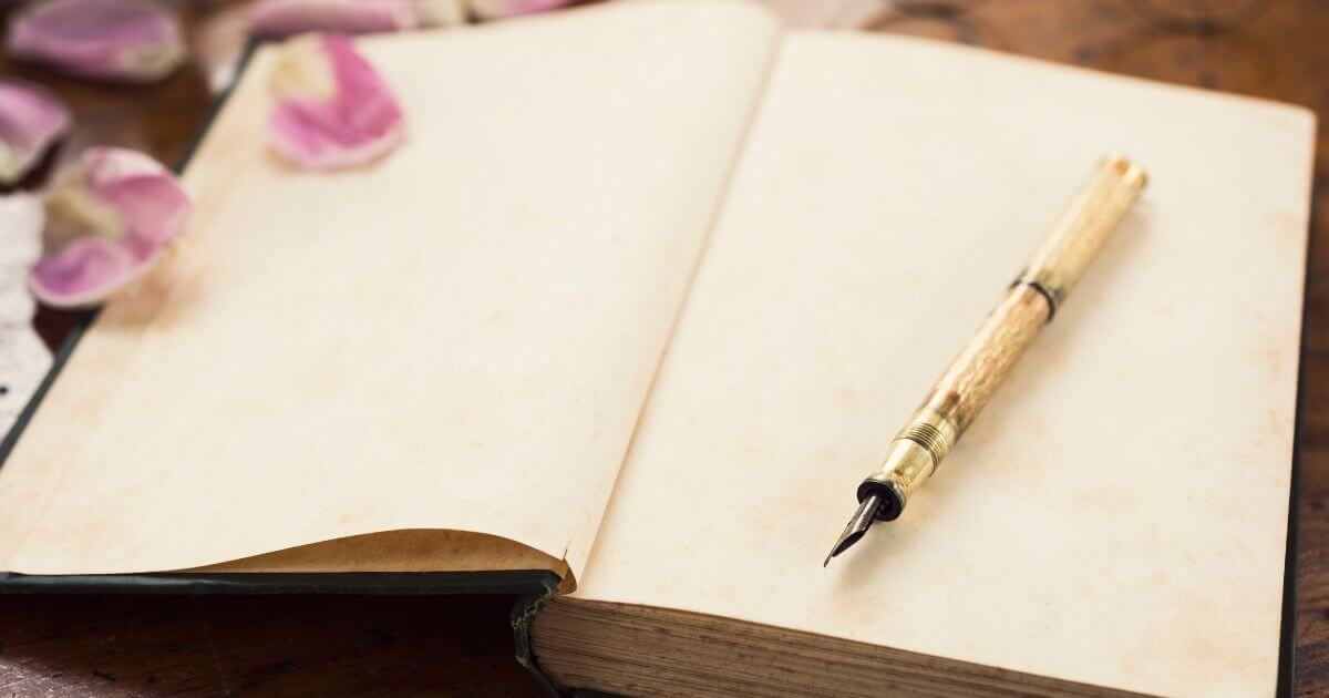 A Dominant's journal sitting on a desk with an antique pen on top of it. The journal is filled with journal prompts for Dominants.