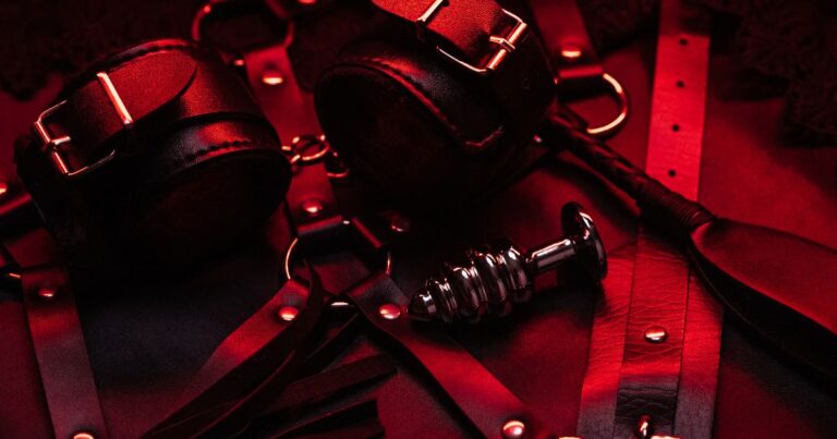Black and red BDSM gear, including restraints and a metal toy, representing power exchange in a D/s relationship.