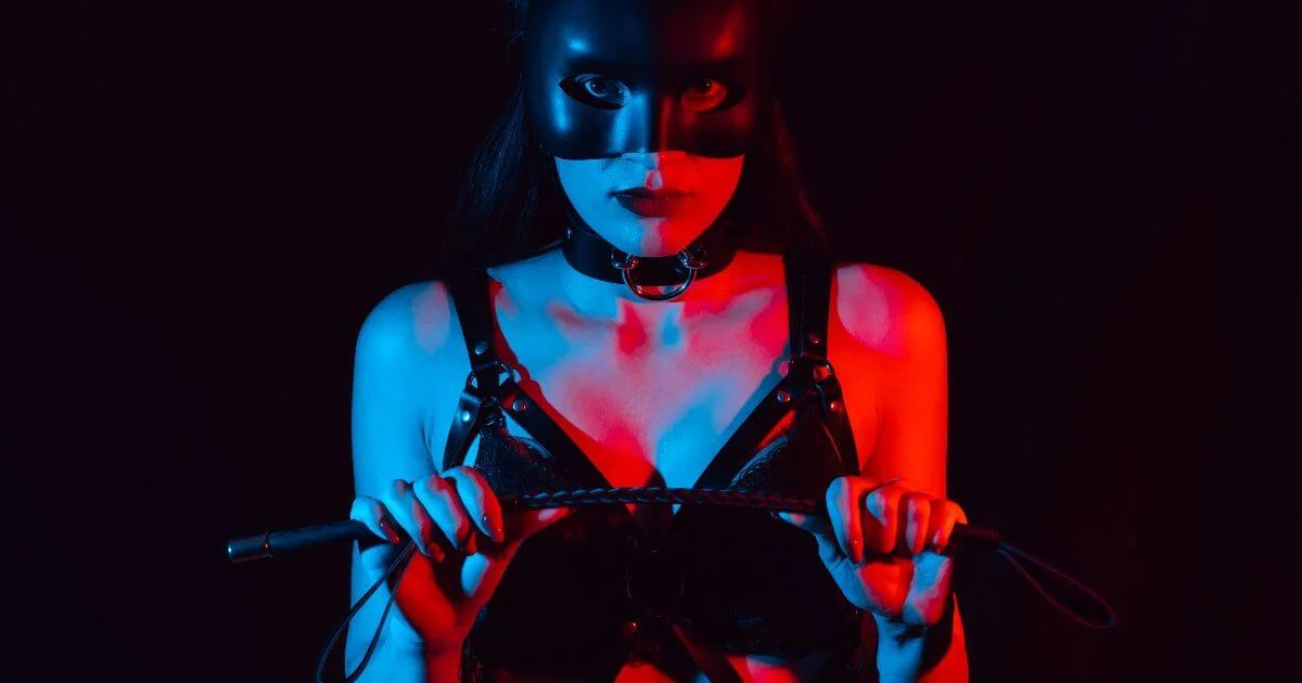 Person wearing BDSM gear and holding a riding crop to represent how to introduce BDSM into a relationship.