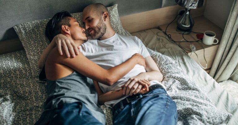 Two partners cuddling in bed after intimacy, representing what is aftercare and the comfort, connection, and support that can follow BDSM play.