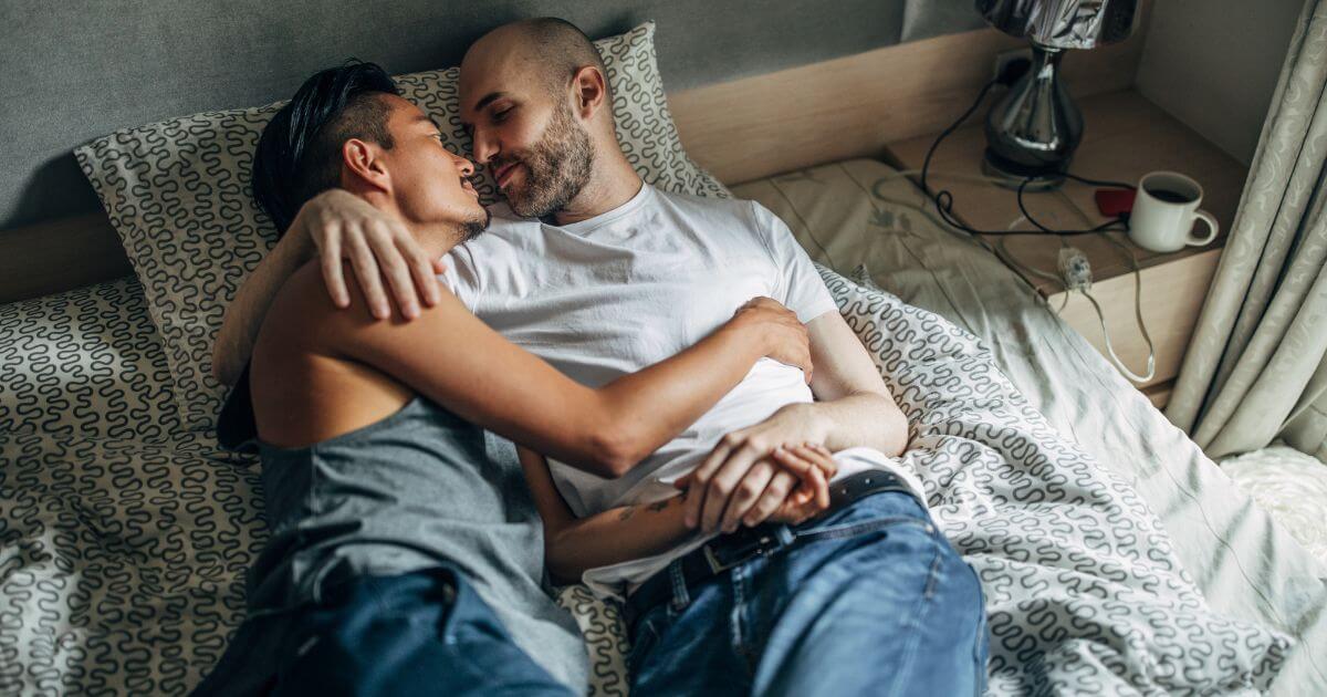 Two partners cuddling in bed after intimacy, representing what is aftercare and the comfort, connection, and support that can follow BDSM play.