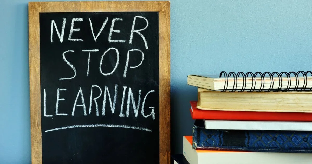 Chalkboard reading “Never Stop Learning” beside a stack of books, representing BDSM education, ongoing learning, and trustworthy kink resources.