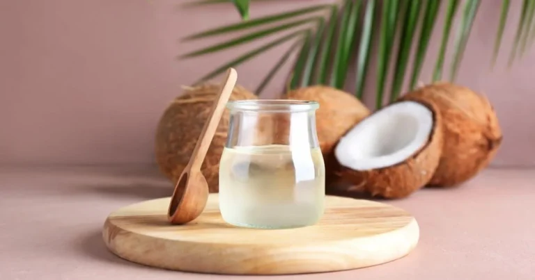 Glass jar of coconut oil with coconuts and a wooden spoon, representing the question “can you use coconut oil as lube?”