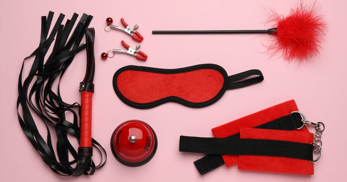Red and black BDSM gear arranged on a pink background to represent BDSM classes and kink education.
