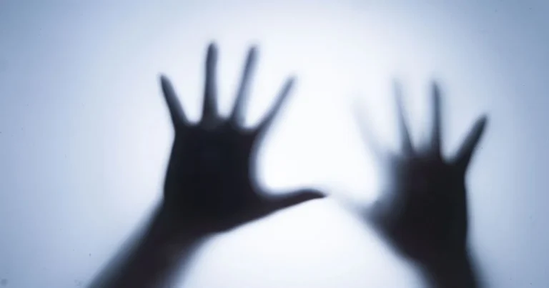 Shadowy hands pressed against a translucent surface, representing BDSM fear play, suspense, vulnerability, and consensual psychological intensity.