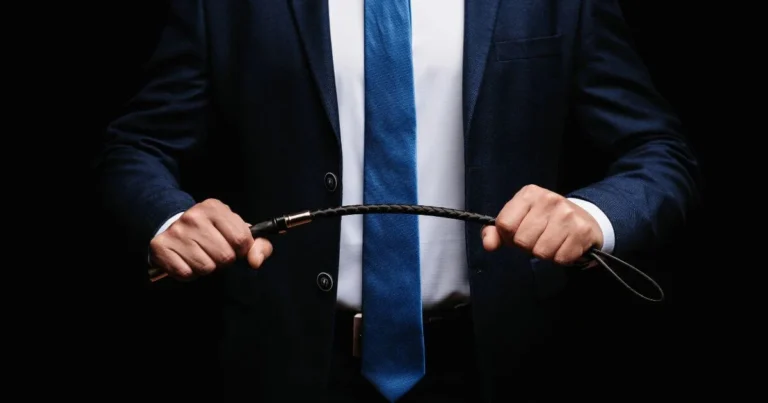 Person in a suit holding a riding crop, representing quotes about dominance, BDSM authority, power, and control.
